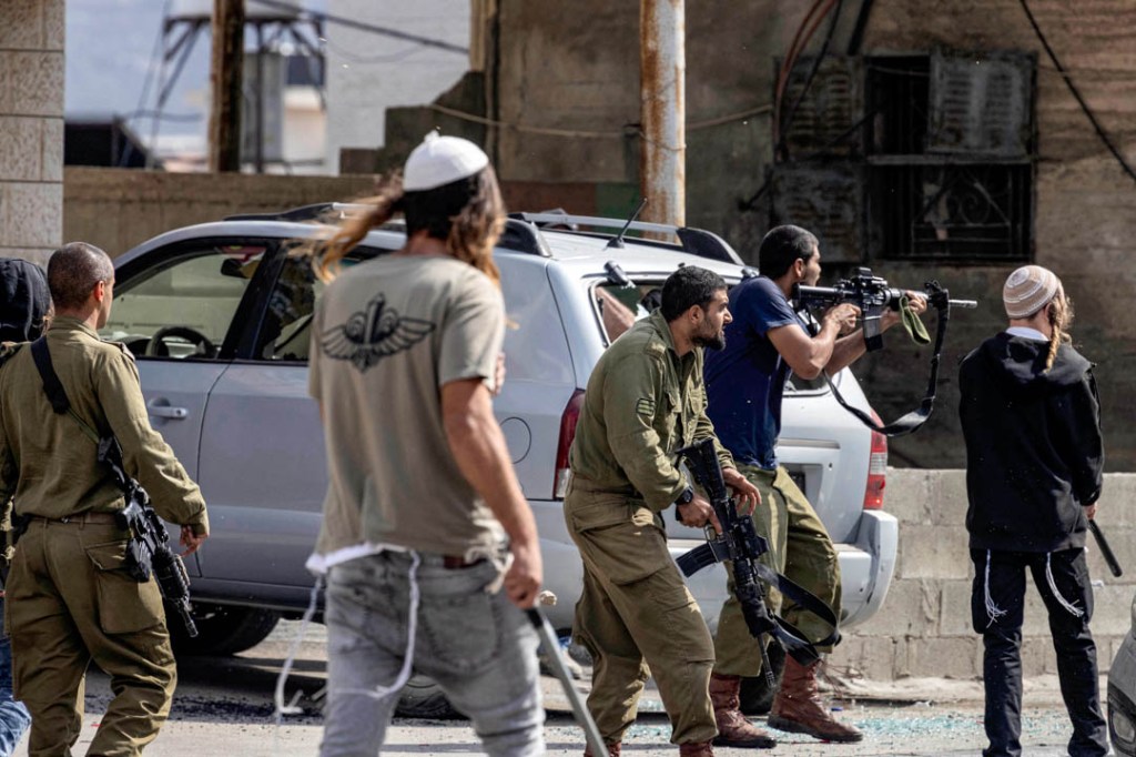 Israeli settlers fire at Palestinians (unseen) while an Israeli soldier (L) stands by during clashes in the town of Huwara in the occupied West Bank on October 13, 2022. (Photo by Oren ZIV / AFP)